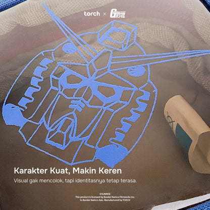 A close-up of a printed decal or sticker featuring a blue line-art illustration of a Gundam-like robot on a brown background, with text and logos including 'torch x' and 'Gundam' visible.