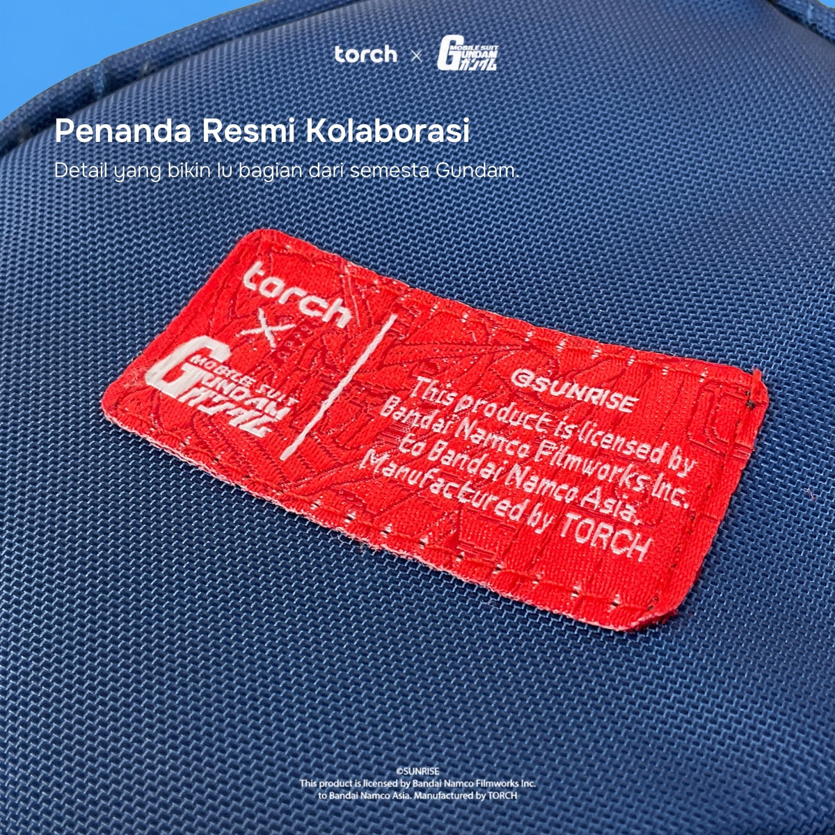 A close-up of a blue woven fabric surface with a prominent red embroidered patch. The patch includes white text reading 'torch x GUNDAM' and additional licensing text, with white overlaid text at the top mentioning a collaboration.