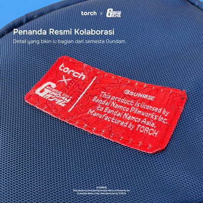 A close-up of a blue woven fabric surface with a prominent red embroidered patch. The patch includes white text reading 'torch x GUNDAM' and additional licensing text, with white overlaid text at the top mentioning a collaboration.