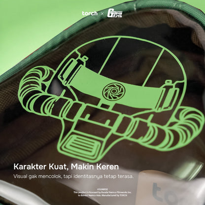 A close-up of a dark green and black backpack or pouch with a neon green line-art graphic of a helmet or mask. White text at the bottom reads 'Karakter Kuat, Makin Keren' with smaller descriptive copy below.